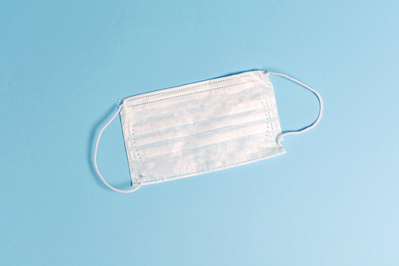 A disposable face mask lying on a light blue surface, symbolizing health protection.